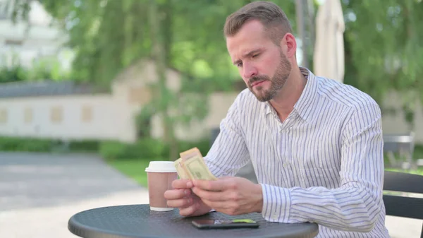 Mature Adult Man Counting Dollars while Sitting in Outdoor Cafe — Stockfoto