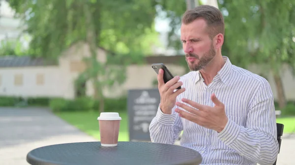 Hombre adulto maduro enojado hablando por teléfono en el café al aire libre — Foto de Stock