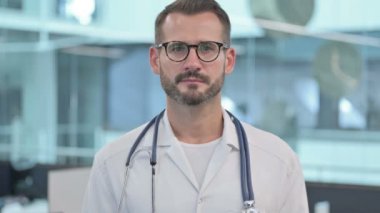 Orta yaşlı erkek doktor kameraya bakıyor. 