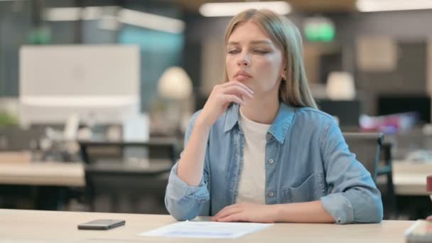 Унылая молодая женщина, сидящая в офисе и думающая — стоковое видео