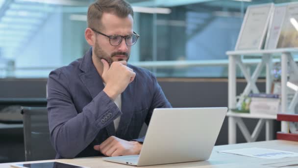 Uomo d'affari di mezza età che pensa mentre lavora al computer portatile in ufficio — Video Stock