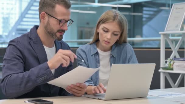 Homme d'affaires et femme d'affaires lisant des documents tout en utilisant un ordinateur portable — Video