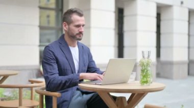 Dışarıdaki kafede oturan adam dizüstü bilgisayarda çalışıyor. 