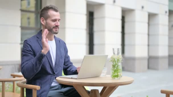 Hombre hablando en videollamada en el ordenador portátil, sentado en el café al aire libre — Vídeos de Stock