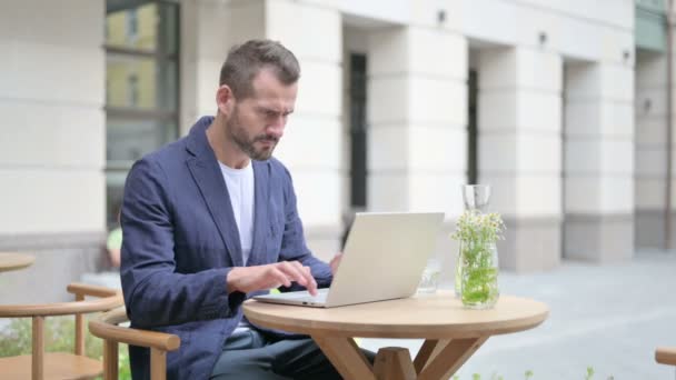 Muž reagující na ztrátu při používání notebooku, sedí v venkovní kavárně — Stock video