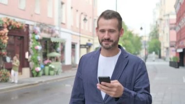 Güzel caddede yürürken telefonu kullanan adam.