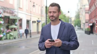 Güzel caddede yürürken telefonu kullanan adam.