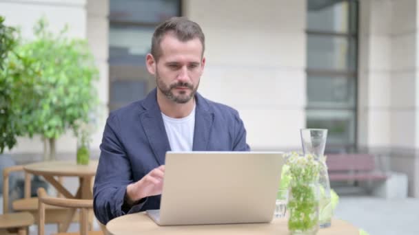 Чоловік розмовляє на відеозв'язку на ноутбуці, сидить у відкритому кафе — стокове відео