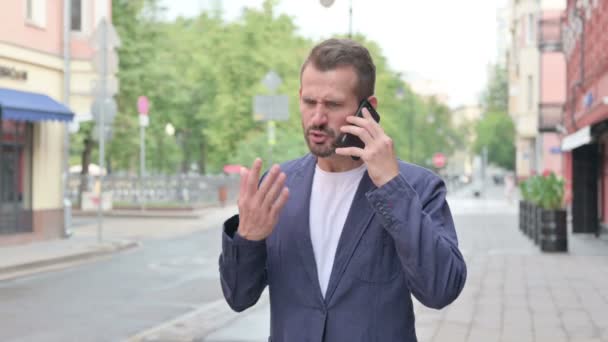 Mann wird bei Telefonat wütend, während er die Straße hinunterläuft — Stockvideo