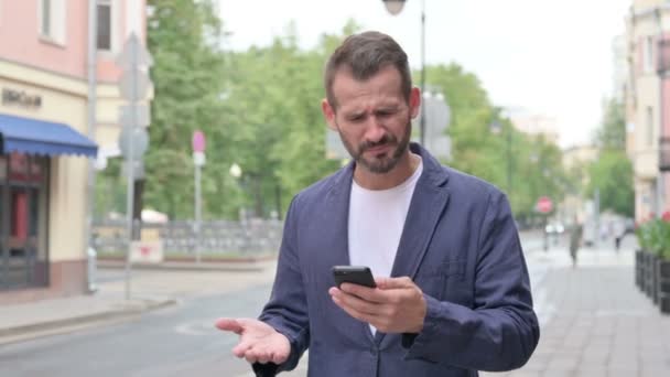 Man Reacting to Loss on Phone while Walking Down the Street — Stock Video