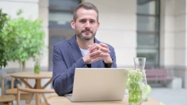 Adam dışarıda dizüstü bilgisayar kullanırken kameraya gülümsüyor