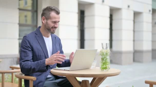 Hombre celebrando mientras usa el ordenador portátil, sentado en el café al aire libre en el banco — Vídeos de Stock