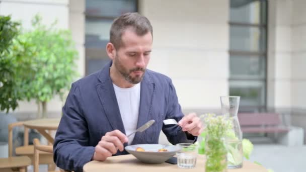 Ο άνθρωπος τρώει μεσημεριανό ενώ κάθεται, κάθεται σε υπαίθριο καφέ — Αρχείο Βίντεο
