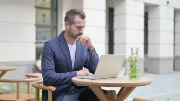 Hombre pensando mientras usa el ordenador portátil, sentado en el café al aire libre — Vídeos de Stock