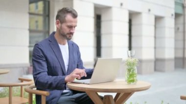 Laptop 'ta çalışırken su içen adam, açık kafede oturan adam.