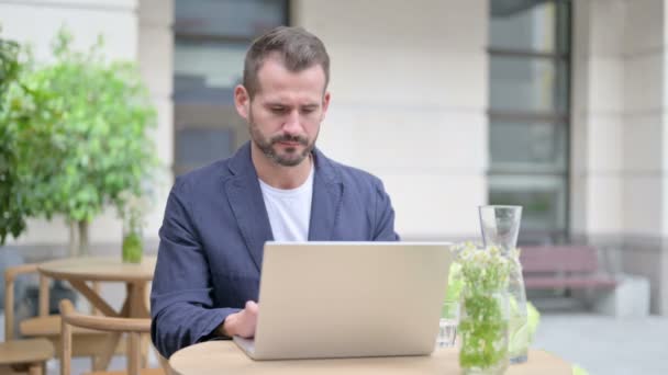 Homme avec mal de tête travaillant sur ordinateur portable, assis dans un café en plein air — Video