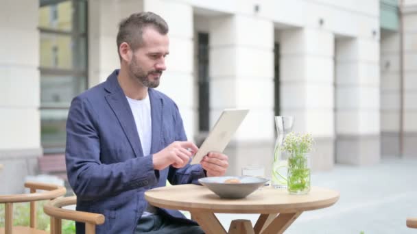 Людина святкує успіх на планшеті, сидячи в кафе на вулиці — стокове відео