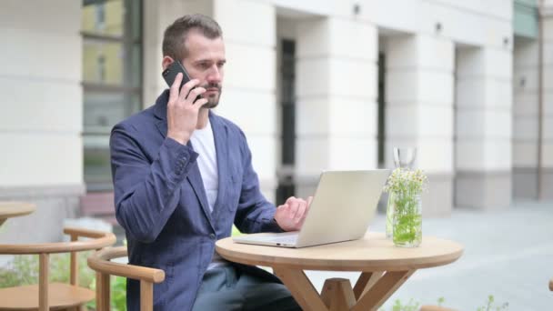 Homem falando em Smartphone enquanto estiver usando Laptop — Vídeo de Stock