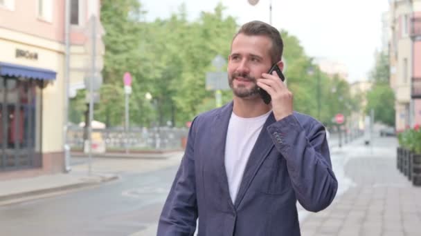 Человек разговаривает по телефону, идя по улице — стоковое видео