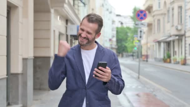Man firar framgång på telefon när du går längs gatan — Stockvideo