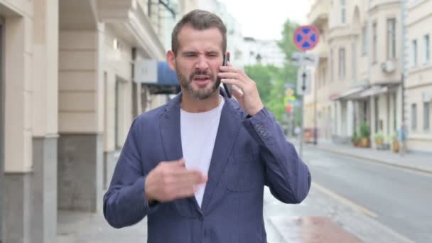 Muž mluví na telefonu zlostně při chůzi po ulici — Stock video