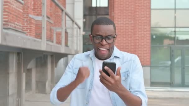 Africký muž slaví úspěch na Smartphone při chůzi v ulici — Stock video