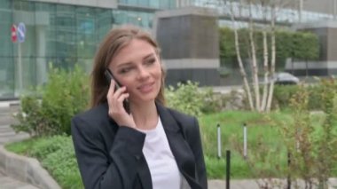 İş kadını sokakta yürürken telefonla konuşuyor.