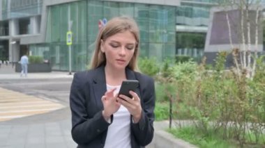 Genç iş kadını sokakta yürürken akıllı telefon kullanıyor.