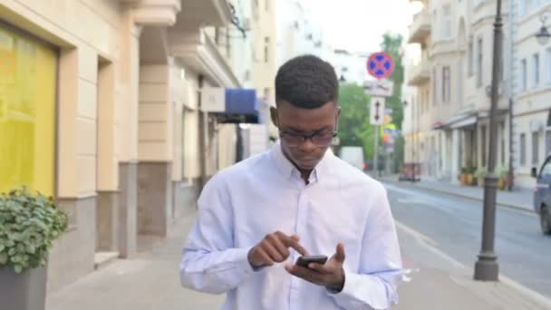 Afrikaanse Man met behulp van Smartphone tijdens het lopen op straat — Stockvideo