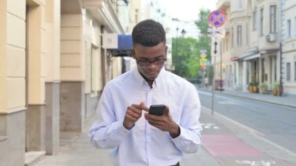 Afrikaanse man viert succes op smartphone tijdens het wandelen op straat — Stockvideo