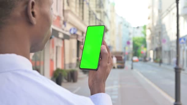 Achteraanzicht van Afrikaanse Man Kijkend naar Smartphone met Green Chroma Screen — Stockvideo