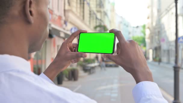 Rückansicht eines Afrikaners, der auf Smartphone mit grünem Chroma-Bildschirm blickt — Stockvideo