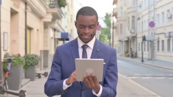 Afrikaanse zakenman werken aan tablet tijdens het lopen op straat — Stockvideo