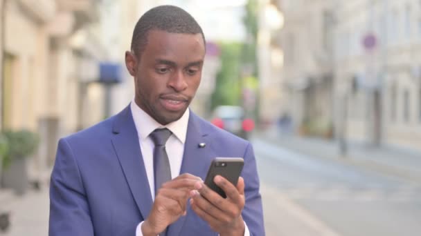Utomhus afrikansk affärsman Fira på smartphone — Stockvideo