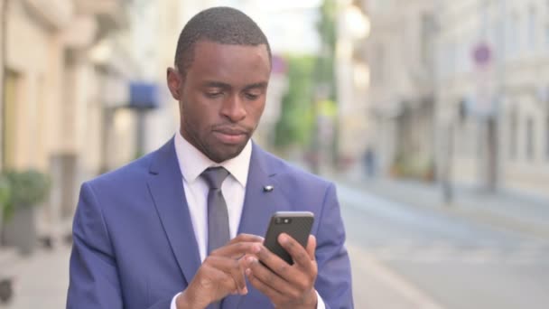 Hombre de negocios africano al aire libre que tiene pérdida en el teléfono inteligente — Vídeos de Stock