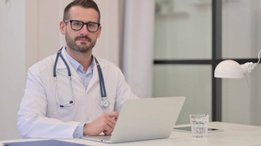 Bilgisayarlı orta yaşlı doktor hastanedeki kameraya bakıyor.