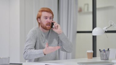 Kızgın genç sakallı kızıl saçlı adam iş yerinde Smartphone 'da konuşuyor. 