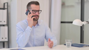 Orta yaşlı adam iş yerinde akıllı telefondan konuşuyor. 