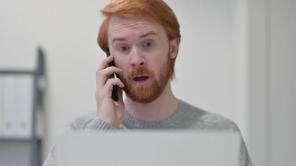 Homem ruivo barba com laptop conversando no smartphone — Fotografia de Stock