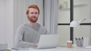 Dizüstü bilgisayarlı kızıl saçlı sakallı adam Evet Hareketi yapıyor 