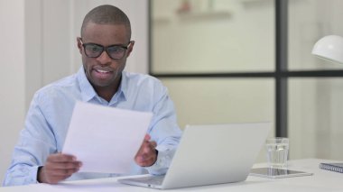 Belgeleri okuyan ve dizüstü bilgisayarda çalışan Afrikalı adam. 