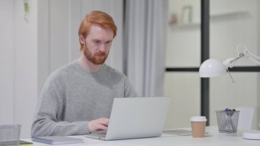 Ofisteki laptopta çalışan kızıl sakallı adam. 