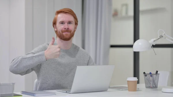 Pollici su da giovane barba rossa uomo con computer portatile al lavoro — Foto Stock