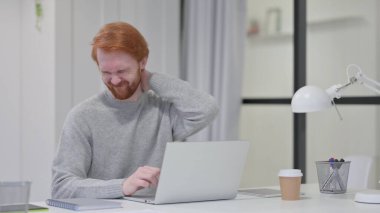 Kırmızı Sakallı Adam dizüstü bilgisayarda yazarken boynu ağrıyor. 