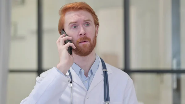 Рыжеволосый врач разговаривает по смартфону на работе — стоковое фото
