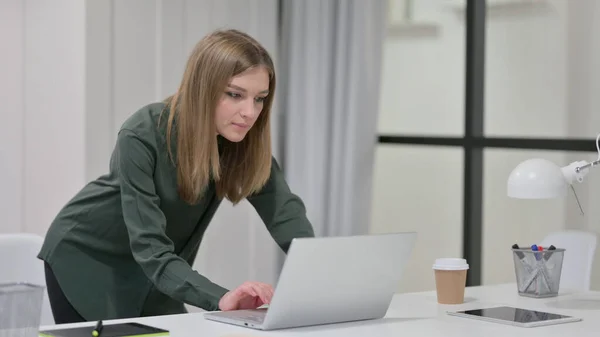 Jovem mulher de pé enquanto usa laptop no trabalho — Fotografia de Stock