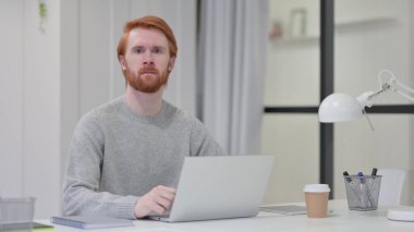Dizüstü bilgisayarlı Sakallı Kızıl Adam İş Başında Kameraya Bakıyor 