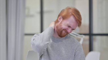 Kızıl saçlı genç sakallı adamın boynu ağrıyor.