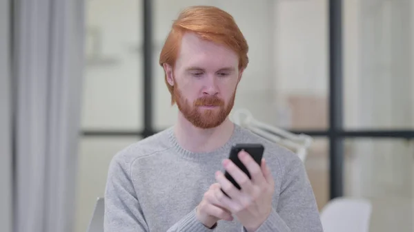 スマートフォンを使用して若いひげの赤毛の男 — ストック写真