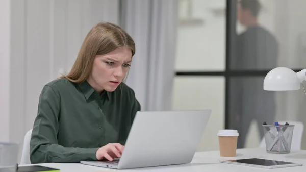 Jovem mulher irritada ao usar laptop no trabalho — Fotografia de Stock